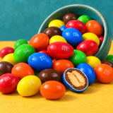 Peanut M&M's spilling from a teal bowl, one candy cut open showing the peanut