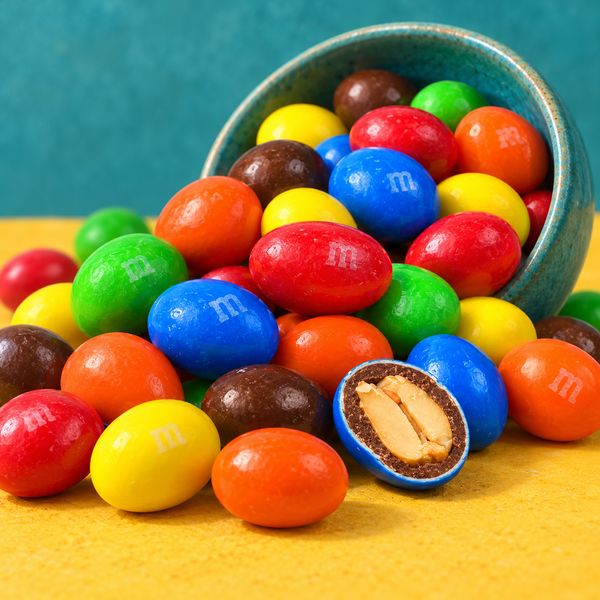 Peanut M&M's spilling from a teal bowl, one candy cut open showing the peanut