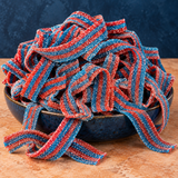 Blazpberry Sour Belts in a bowl, chewy red-and-blue striped sour candy strips coated in sour sugar